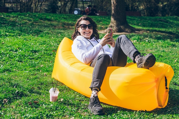 Jeune jolie femme sur un matelas gonflable jaune dans le parc de la ville surfant au téléphone