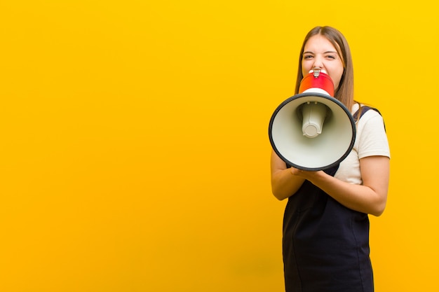 Jeune jolie femme avec un mégaphone contre le mur orange