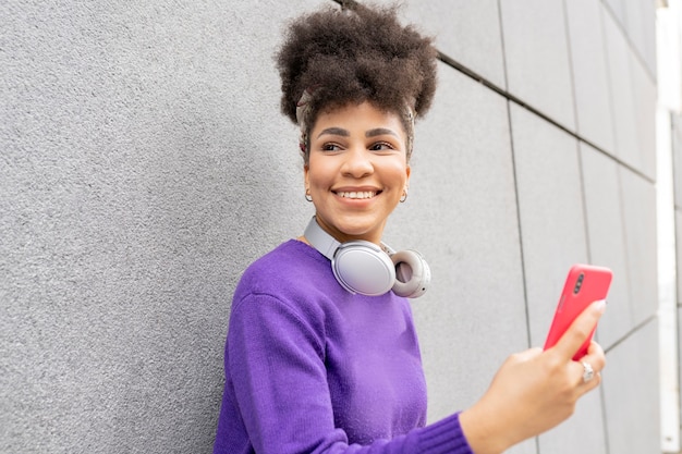 Jeune jolie femme, métisse afro, dans la rue avec un casque et un smartphone happy smiling,