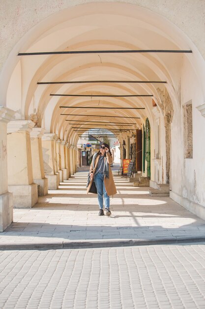 Jeune jolie femme à la mode marchant dans un manteau marron par la rue de la ville