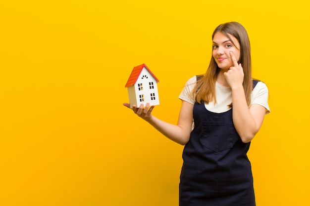 Jeune jolie femme avec un modèle de maison sur fond orange