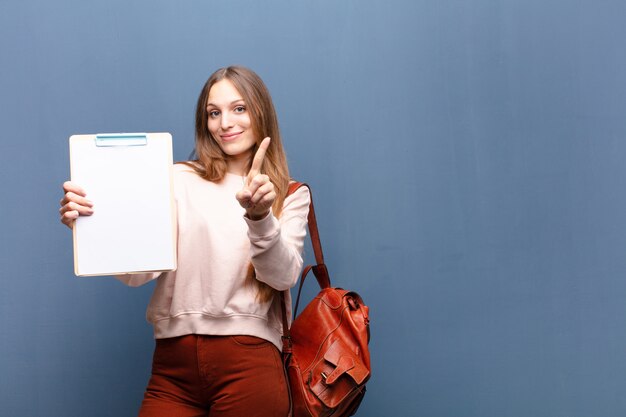 Jeune jolie femme avec un morceau de papier contre le mur bleu avec un espace de copie