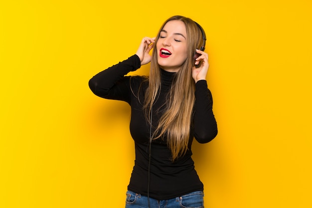 Jeune jolie femme sur un mur jaune, écouter de la musique avec des écouteurs