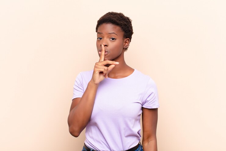 Photo jeune jolie femme noire demandant le silence et le calme, faisant des gestes avec le doigt devant la bouche, disant chut ou gardant un secret