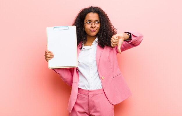 Jeune jolie femme noire avec une feuille de papier contre le mur rose