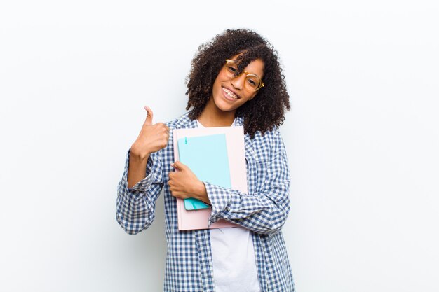 Jeune jolie femme noire avec des livres contre le mur blanc