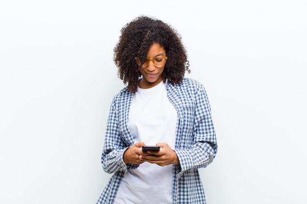 Jeune jolie femme noire avec un téléphone intelligent contre un mur blanc