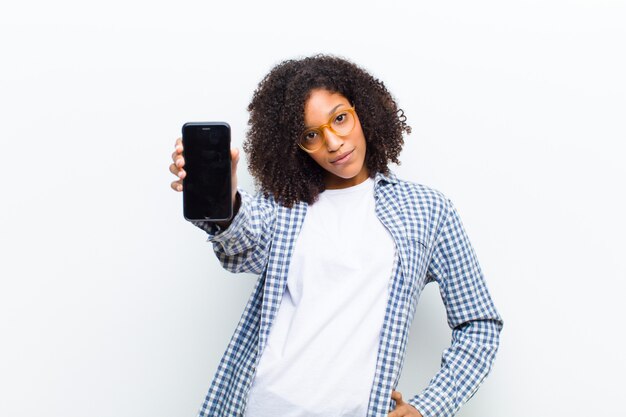 Jeune jolie femme noire avec un téléphone intelligent contre un mur blanc