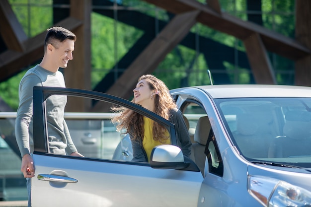 Jeune jolie femme ouvrant la portière de la voiture et parlant au jeune homme