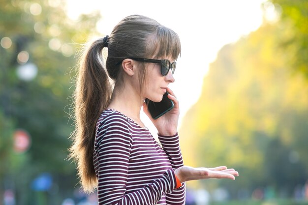 Jeune jolie femme parlant au téléphone portable par une chaude journée d'automne dans une rue de la ville à l'extérieur.