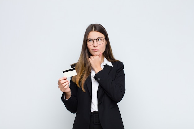 Jeune jolie femme pensant, douteuse et confuse, avec différentes options, se demandant quelle décision prendre avec une carte de crédit