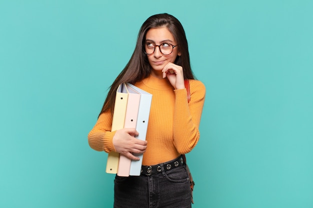 Jeune jolie femme pensant, se sentant dubitative et confuse, avec différentes options, se demandant quelle décision prendre. concept d'étudiant