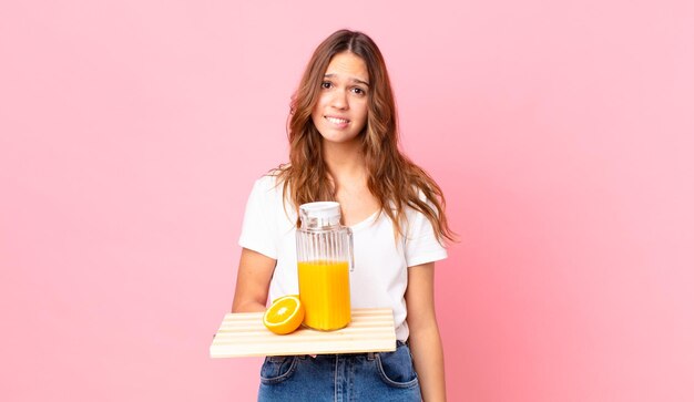 Jeune jolie femme à la perplexité et confuse et tenant un plateau avec un jus d'orange