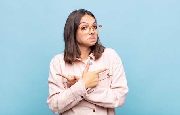 Jeune jolie femme à la perplexité et à la confusion, l'insécurité et pointant dans des directions opposées avec des doutes