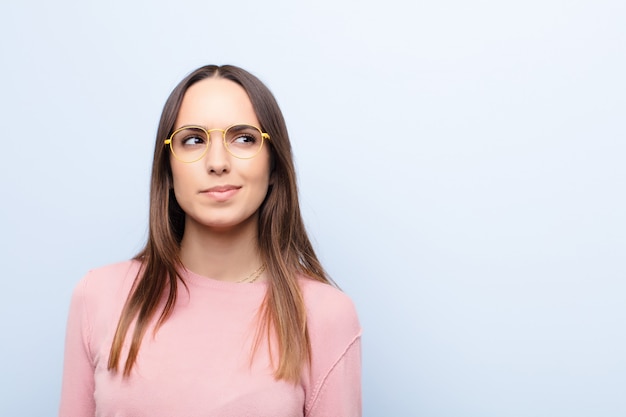 Jeune jolie femme à la perplexité et à la confusion, se demandant ou essayant de résoudre un problème ou réfléchissant au mur bleu