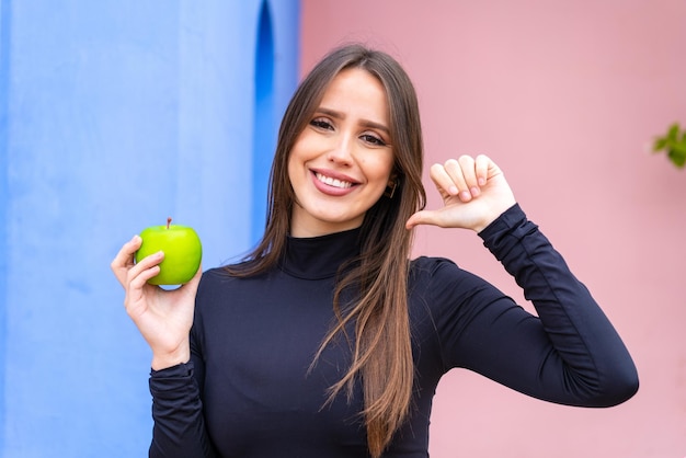 Jeune jolie femme avec une pomme à l'extérieur fière et satisfaite