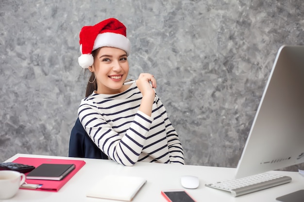 Jeune jolie femme portant un chapeau de Noël travaillant au bureau.