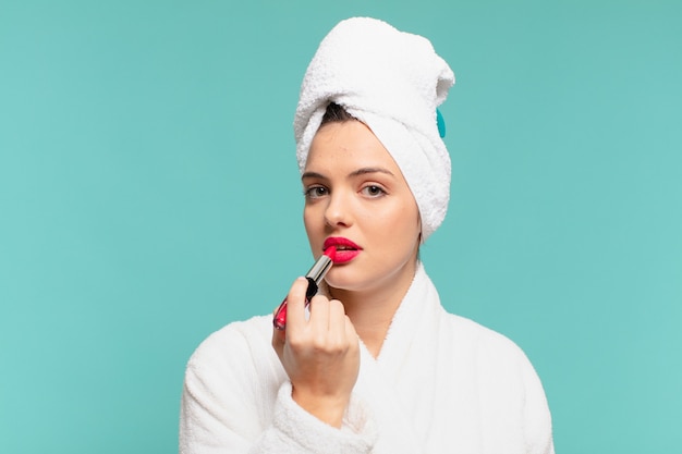 Jeune jolie femme portant une expression heureuse de peignoir et un rouge à lèvres