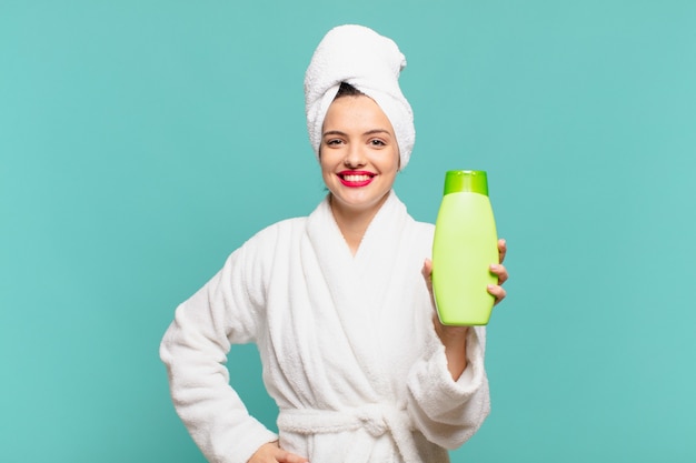 Jeune jolie femme portant un peignoir avec une expression heureuse et un masque facial à l'avocat