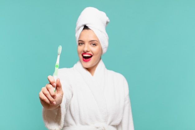 Jeune jolie femme portant un peignoir avec une expression surprise et tenant une brosse à dents