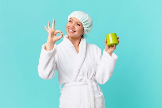 Jeune jolie femme portant un peignoir et tenant une bouteille de produit propre