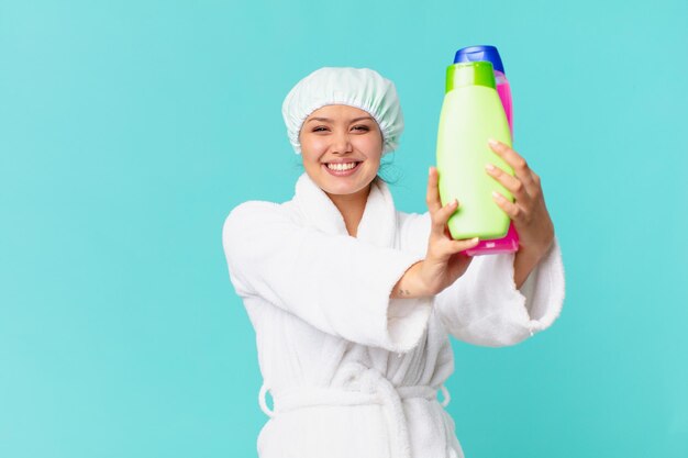 Jeune jolie femme portant un peignoir et tenant une bouteille de produit propre