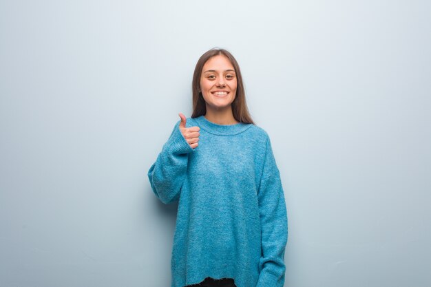 Jeune jolie femme portant un pull bleu souriant et levant le pouce vers le haut