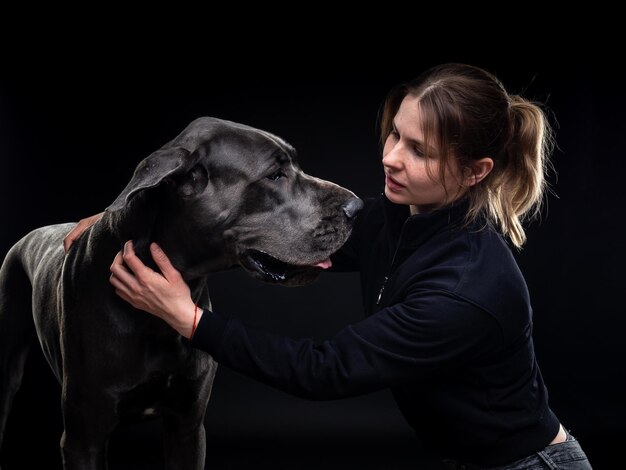 Jeune jolie femme pose avec son animal de compagnie un Dogue Allemand mis en évidence sur un fond noir