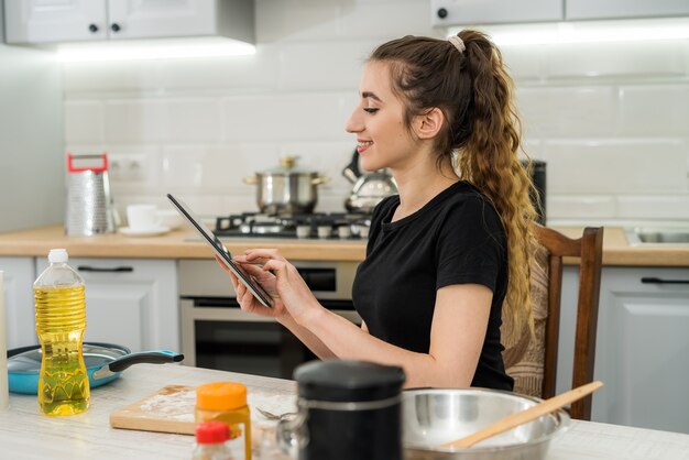 Jeune jolie femme préparant des cookies à la maison avec aide tablette numérique. Fait maison