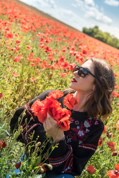 Jeune jolie femme profitant de l'heure d'été dans le champ de fleurs de coquelicots. liberté