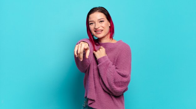 Jeune jolie femme avec pull rose posant sur un mur turquoise