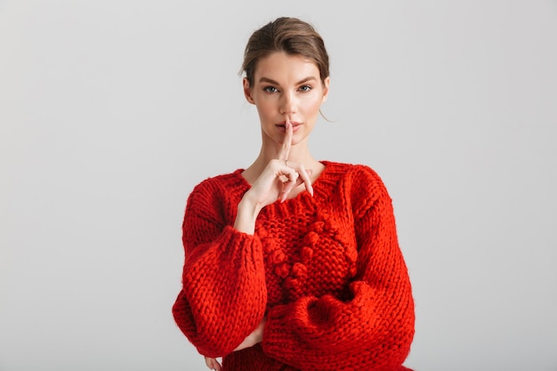 Jeune jolie femme en pull rouge montrant le geste de silence directement isolé sur fond blanc