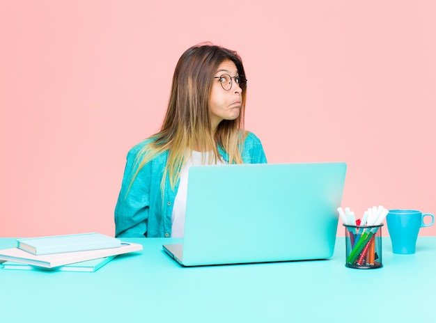 Jeune jolie femme qui travaille avec un ordinateur portable avec une expression maladroite, folle et surprise, des joues bouffantes, se sentant bourrée, grasse et pleine de nourriture