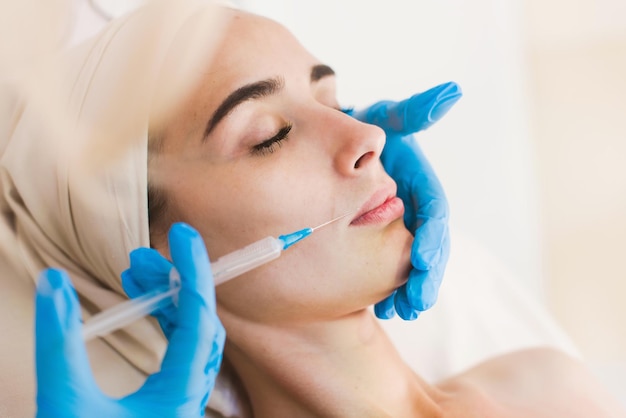 Jeune jolie femme recevant des traitements dans des salons de beauté. Belle jeune femme brune dans l'esthéticienne de bureau allongée sur le canapé. Procédure de remodelage, revitalisation. Injections de beauté.