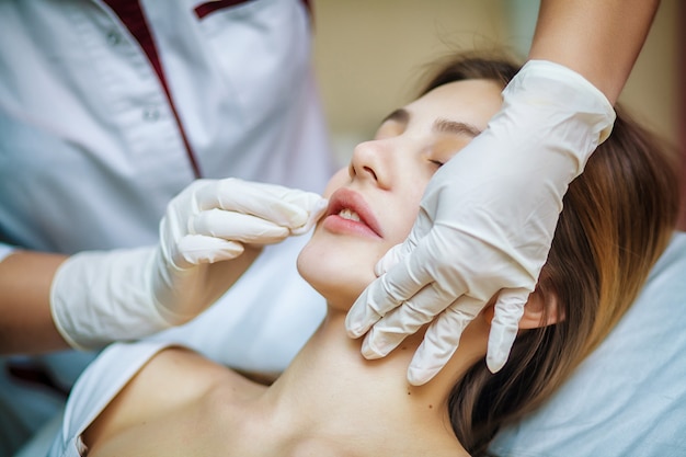 Jeune jolie femme recevant des traitements dans les salons de beauté. Belle jeune femme dans l'esthéticienne de bureau allongé sur le canapé. Procédure de contournage, revitalisation. Injections de beauté.