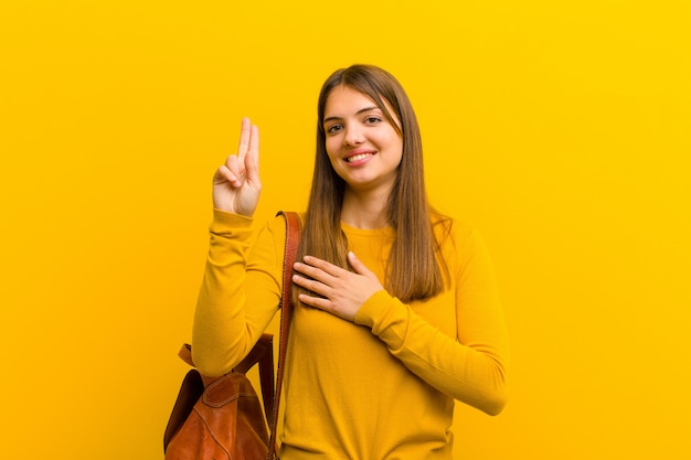 Jeune jolie femme à la recherche de plaisir, confiante et digne de confiance, souriante et montrant le signe de la victoire, avec une attitude positive à l'orange