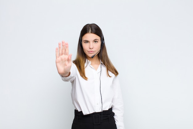 Jeune jolie femme à la recherche de sérieux, sévère, mécontent et en colère montrant la paume ouverte faisant un geste d'arrêt avec un casque et un microphone