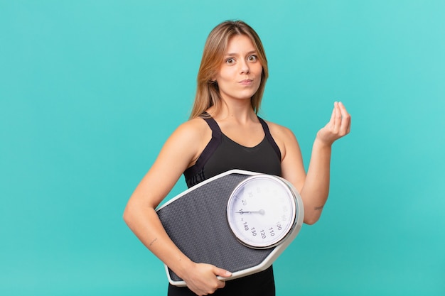 Jeune jolie femme de remise en forme faisant un geste de capice ou d'argent, vous disant de payer