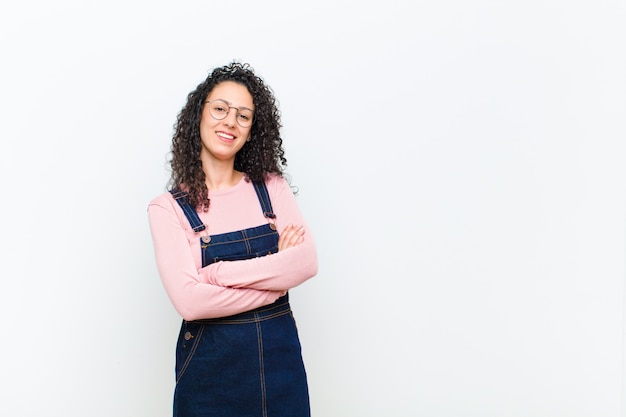 Jeune jolie femme ressemblant à un réalisateur heureux, fier et satisfait souriant avec les bras croisés contre le mur blanc