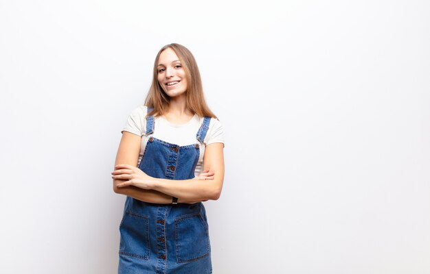 Jeune jolie femme ressemblant à un réalisateur heureux, fier et satisfait souriant avec les bras croisés contre le mur blanc