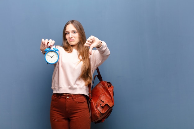 Jeune jolie femme avec un réveil contre le mur bleu avec un espace de copie