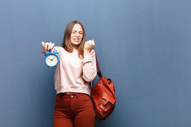 Jeune jolie femme avec un réveil contre le mur bleu avec un espace de copie