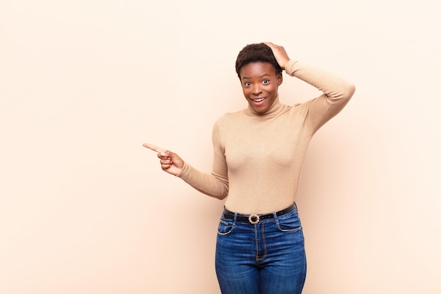 Jeune jolie femme riant, l'air heureux, positif et surpris, réalisant une excellente idée pointant vers l'espace de copie latérale