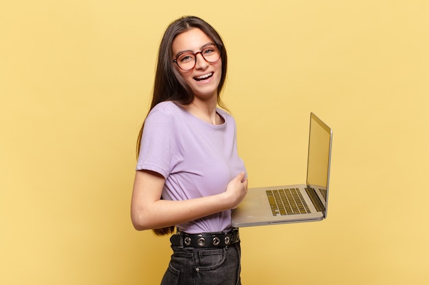 Jeune jolie femme riant aux éclats d'une blague hilarante, se sentant heureuse et joyeuse, s'amusant. concept d'ordinateur portable