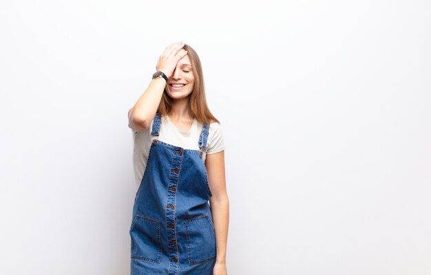 Jeune jolie femme riant et giflant le front comme disant dÃ ¢ Â € ÂšÃƒÂ „ÃƒÂ´oh! J'ai oublié ou c'était une erreur stupide contre un mur blanc