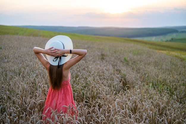 Jeune jolie femme en robe d'été rouge et chapeau de paille debout sur un champ de ferme jaune