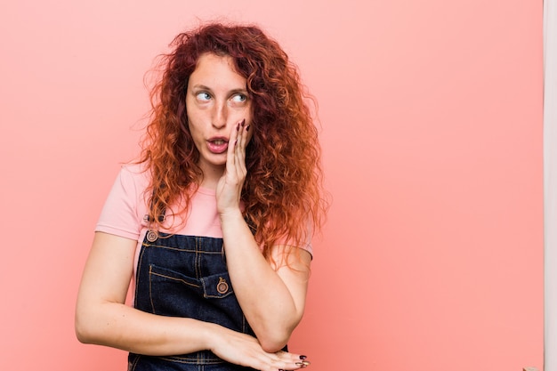 Jeune et jolie femme rousse au gingembre vêtue d'un salopette en jean raconte une chaude nouvelle de freinage et regarde de côté