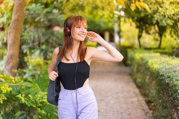 Jeune jolie femme rousse à l'extérieur, écouter de la musique