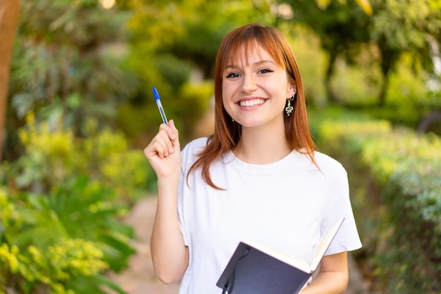 Jeune jolie femme rousse à l'extérieur tenant un cahier