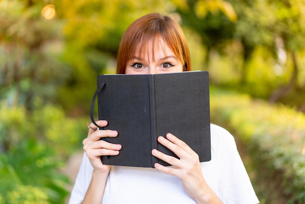 Jeune jolie femme rousse à l'extérieur tenant un cahier